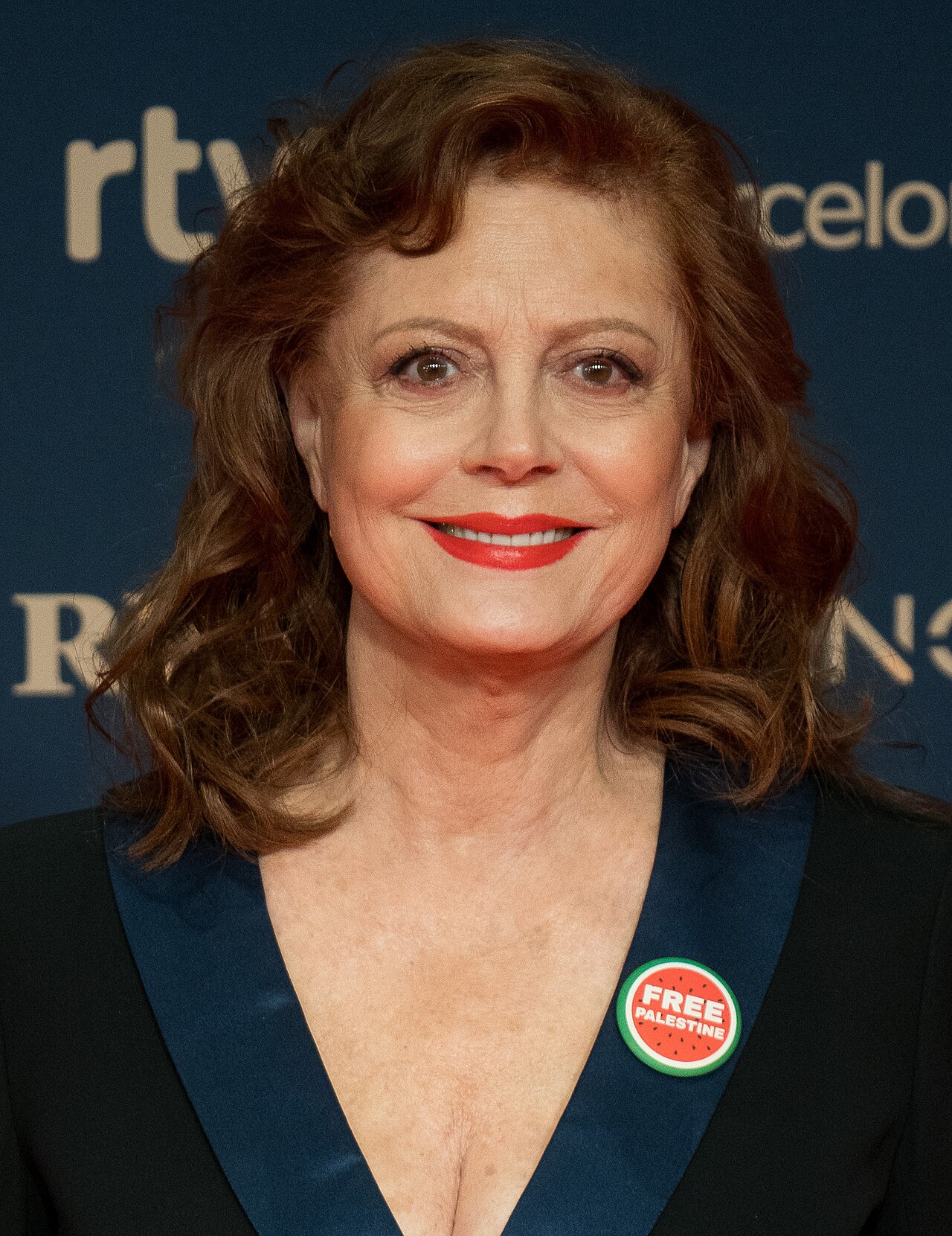 Susan Sarandon smiling on a red carpet, wearing a dark outfit
