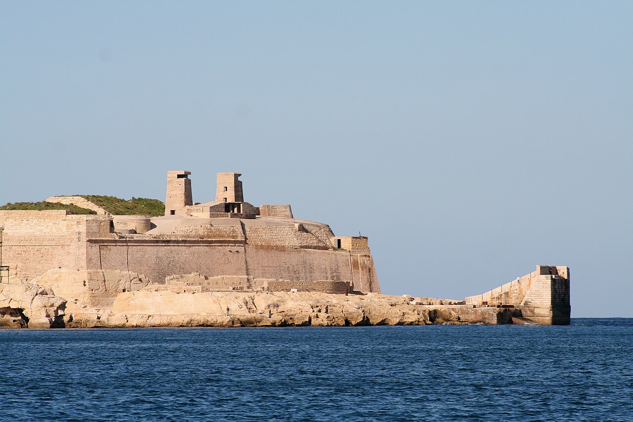 The pale stone walls and towers of Fort St. Elmo rising above the rocky shore, seen across blue water