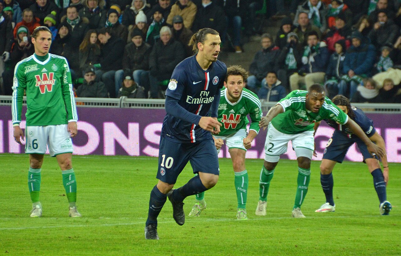 Zlatan Ibrahimović in a dark blue Paris Saint-Germain shirt with the number 10, running toward the ball as opposing players in green wait at the edge of the box